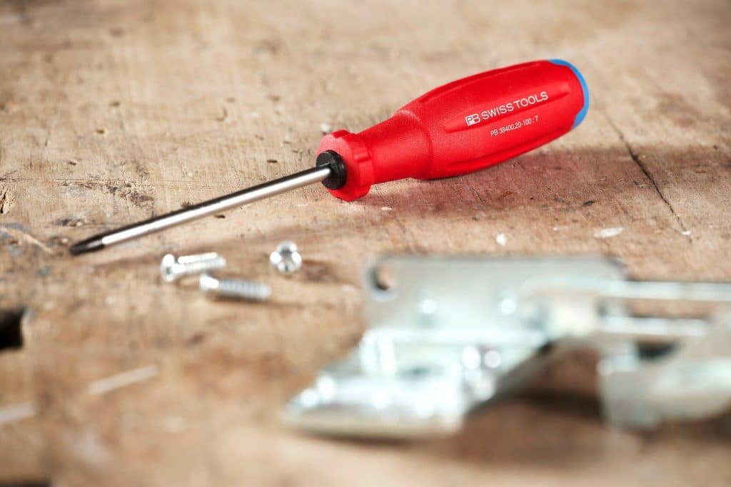 Red handled screwdriver with screws on wooden surface