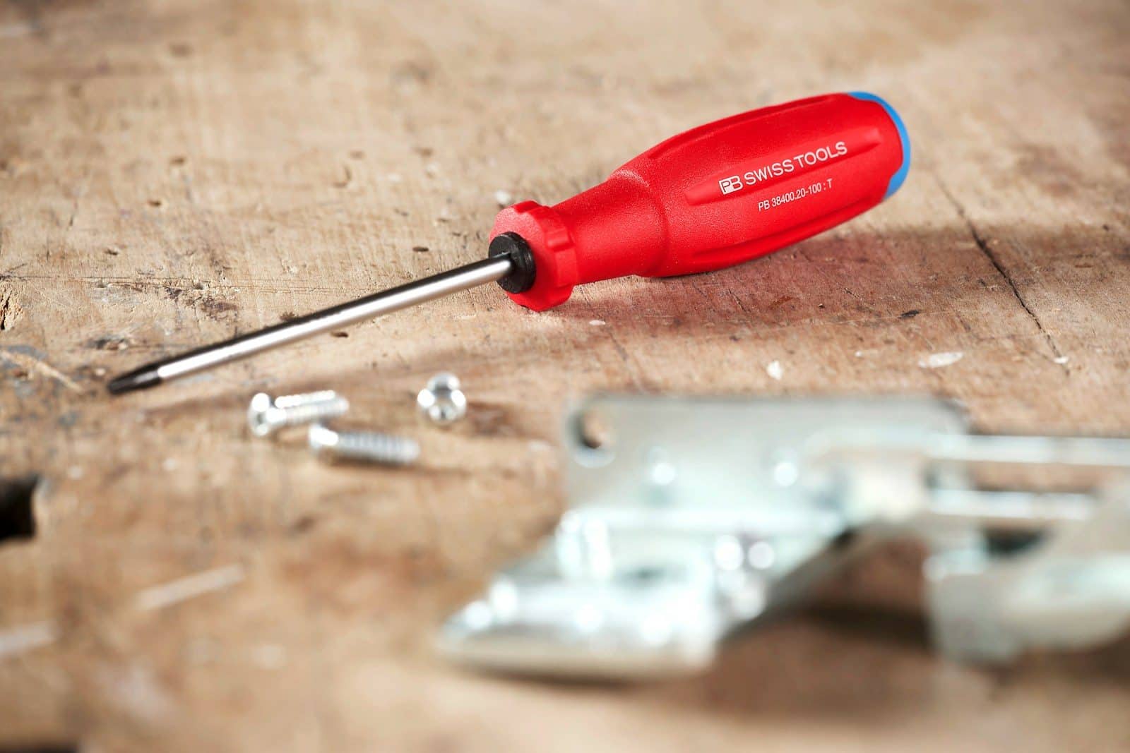 Red handled screwdriver with screws on wooden surface