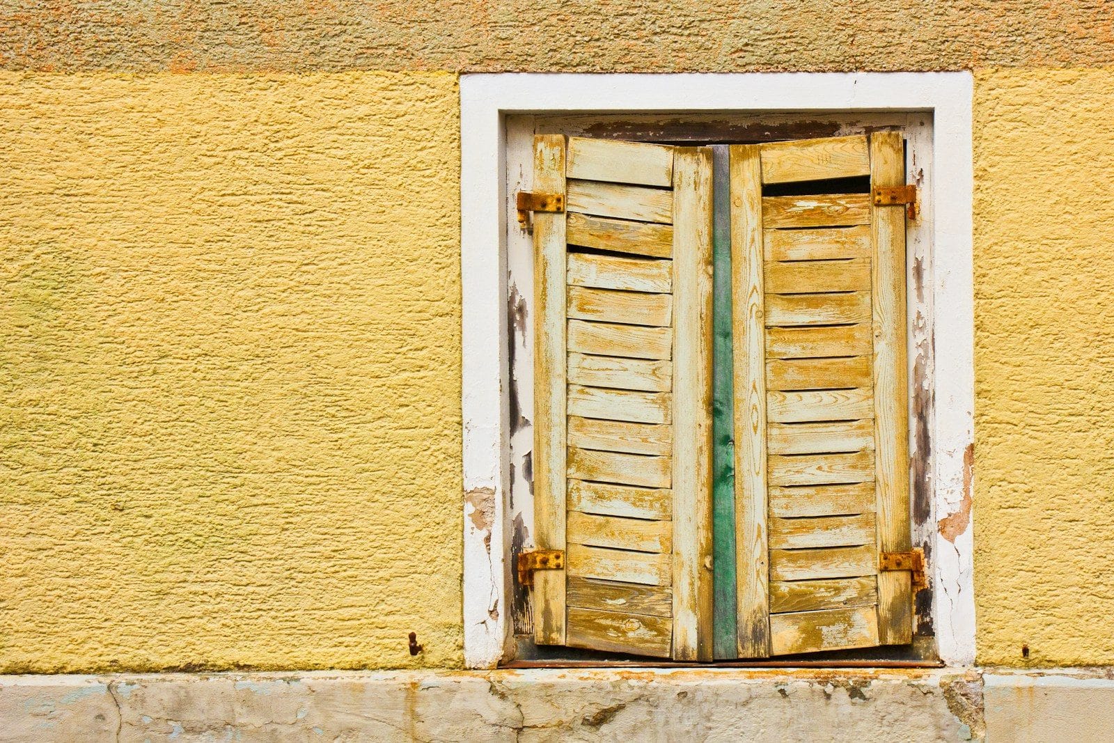 Old, weathered shutters on a yellow wall.